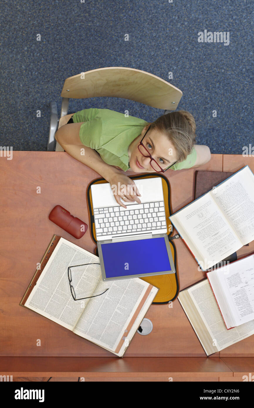Studentessa seduti ad una scrivania con un computer portatile e di libri, vista dall'alto Foto Stock