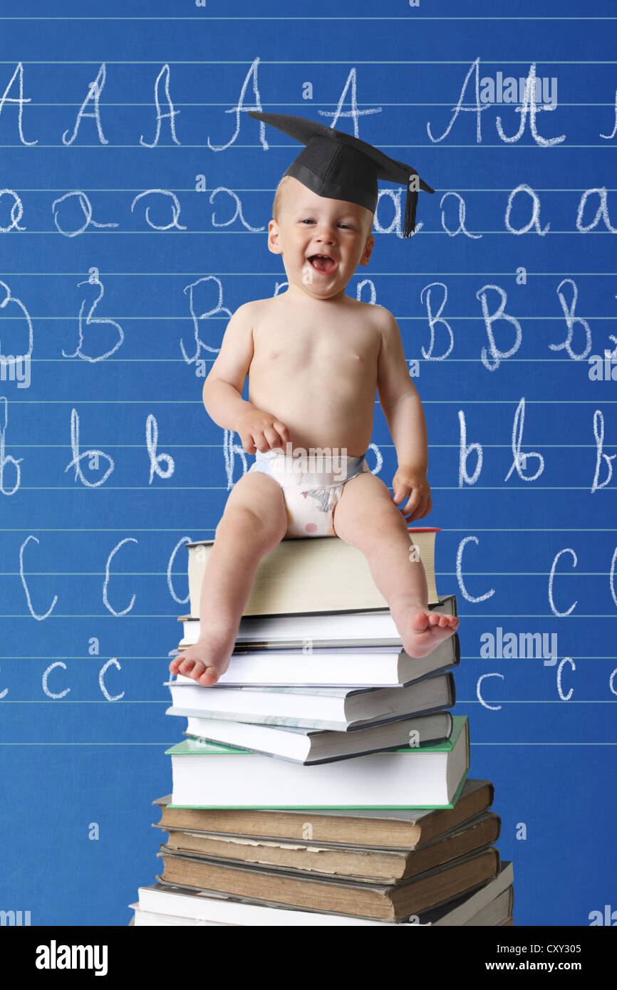Ridere neonato indossando un cappello di graduazione seduto su una pila di libri di fronte a una scuola lavagna con l ABC Foto Stock