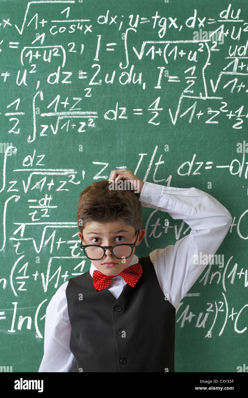 Impotente cercando schoolboy indossando occhiali e un filtro bow tie di fronte a una lavagna con le equazioni matematiche Foto Stock