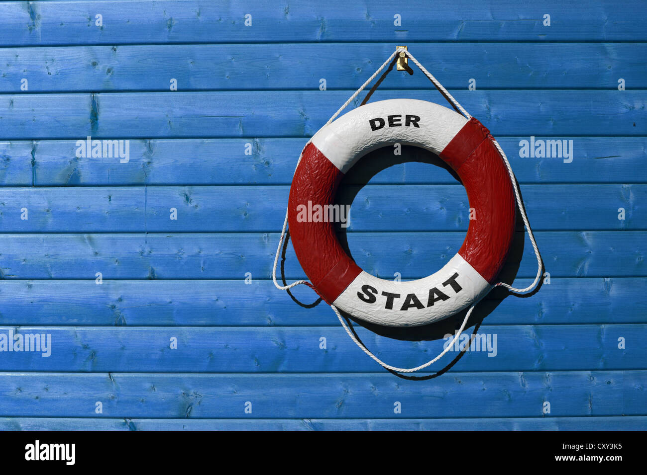 Anello di vita etichettati der Staat, Tedesco per la nazione, appeso su un blu parete in legno Foto Stock