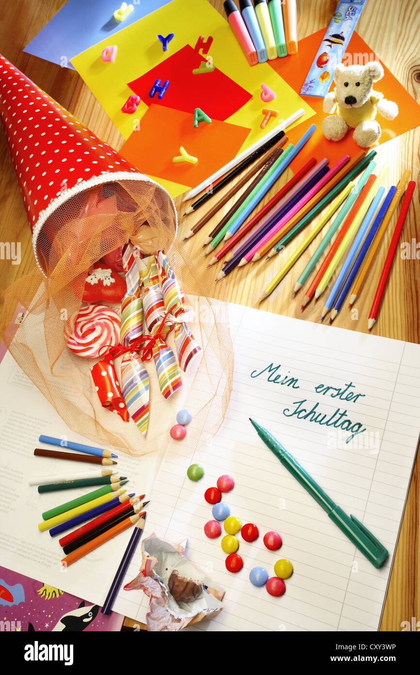 Schultuete o scuola cono riempito con doni e dolciumi accanto a matite colorate e un notebook con la voce Mein erster Foto Stock