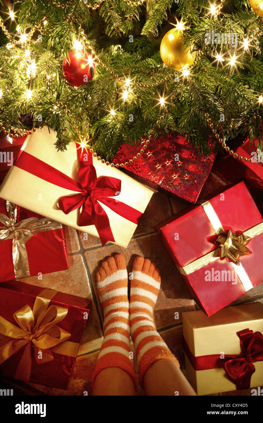 Ragazza, vista in dettaglio, gambe in piedi di fronte a regali di Natale sotto un albero di Natale Foto Stock