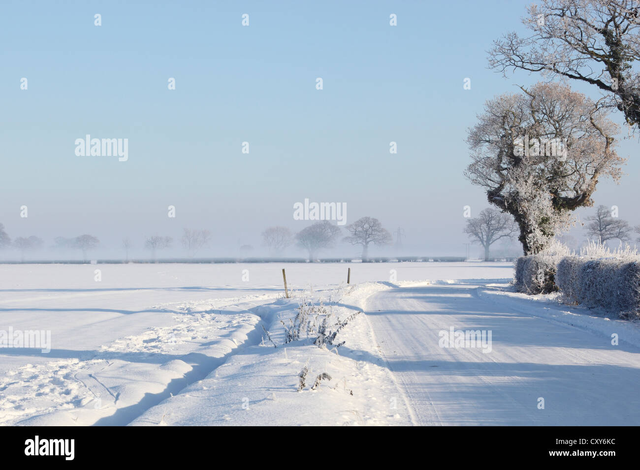 Un paesaggio invernale con una piccola strada di campagna e terreni agricoli coperti di neve profonda Foto Stock