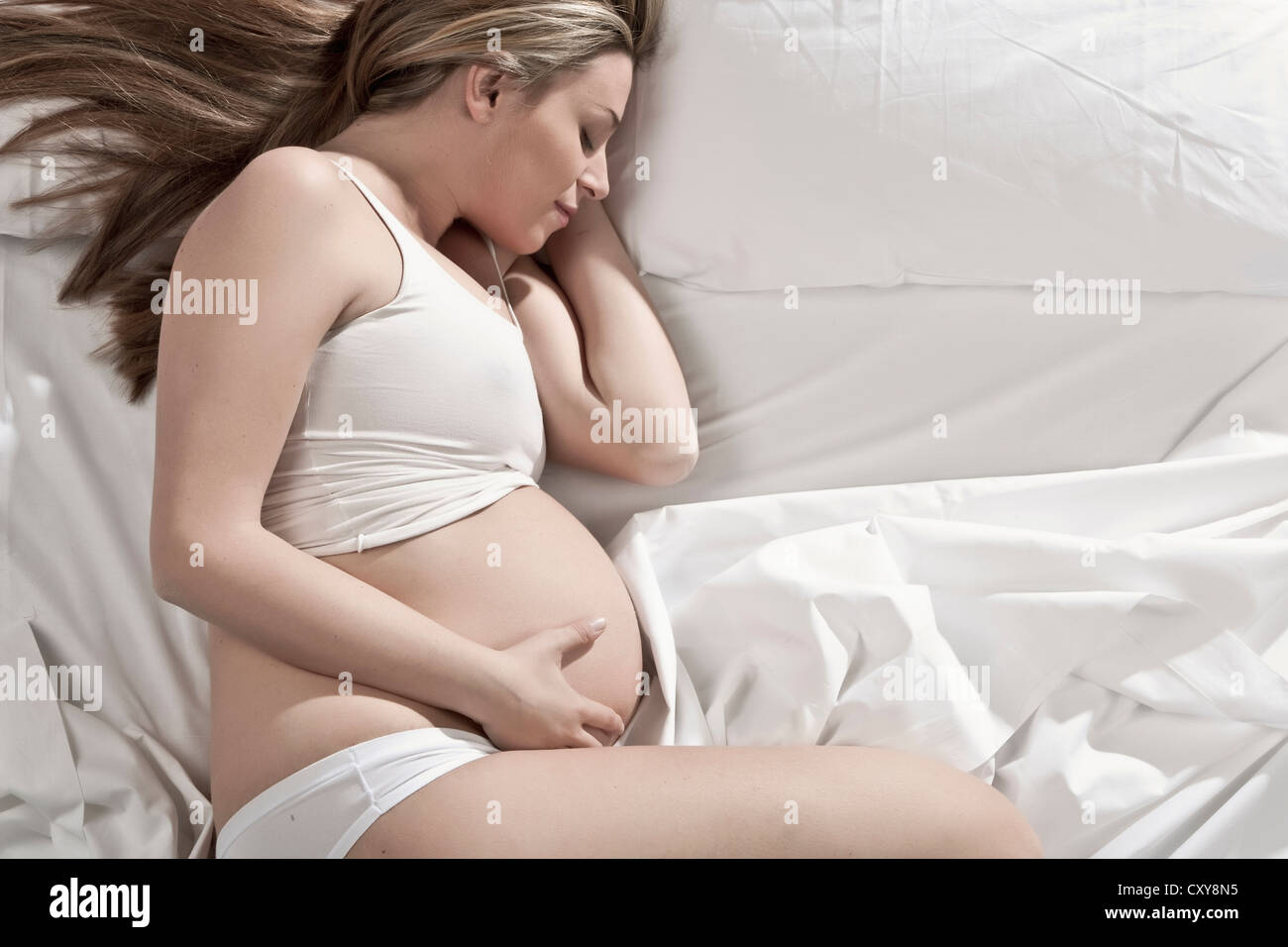 Donna incinta dorme nel letto Foto Stock