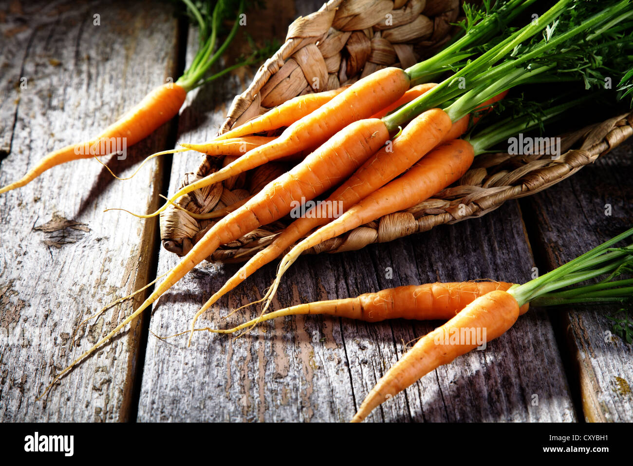 Le carote fresche, carote in un cesto di vimini sul legno rustico Foto Stock