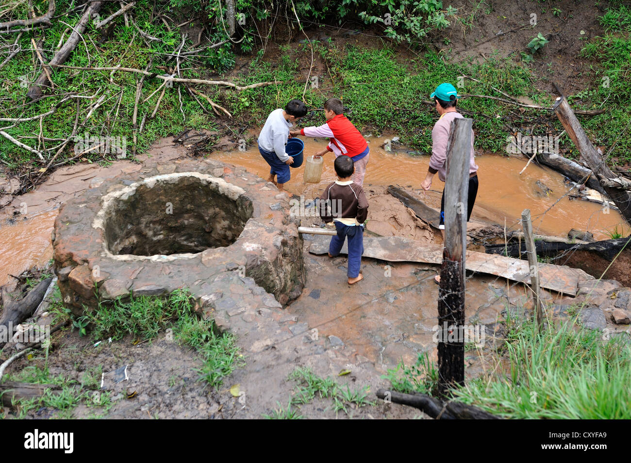 I bambini la raccolta di acqua da un torrente fangoso, Comunida Martillo, Caaguazu, Paraguay, Sud America Foto Stock