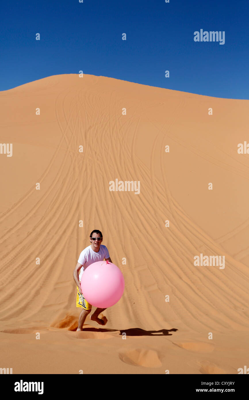 Leggerezza, uomo che porta un grande palloncino rosa nel deserto, Coral Pink Sand Dunes State Park, vicino a Kanab, Utah, Stati Uniti d'America Foto Stock