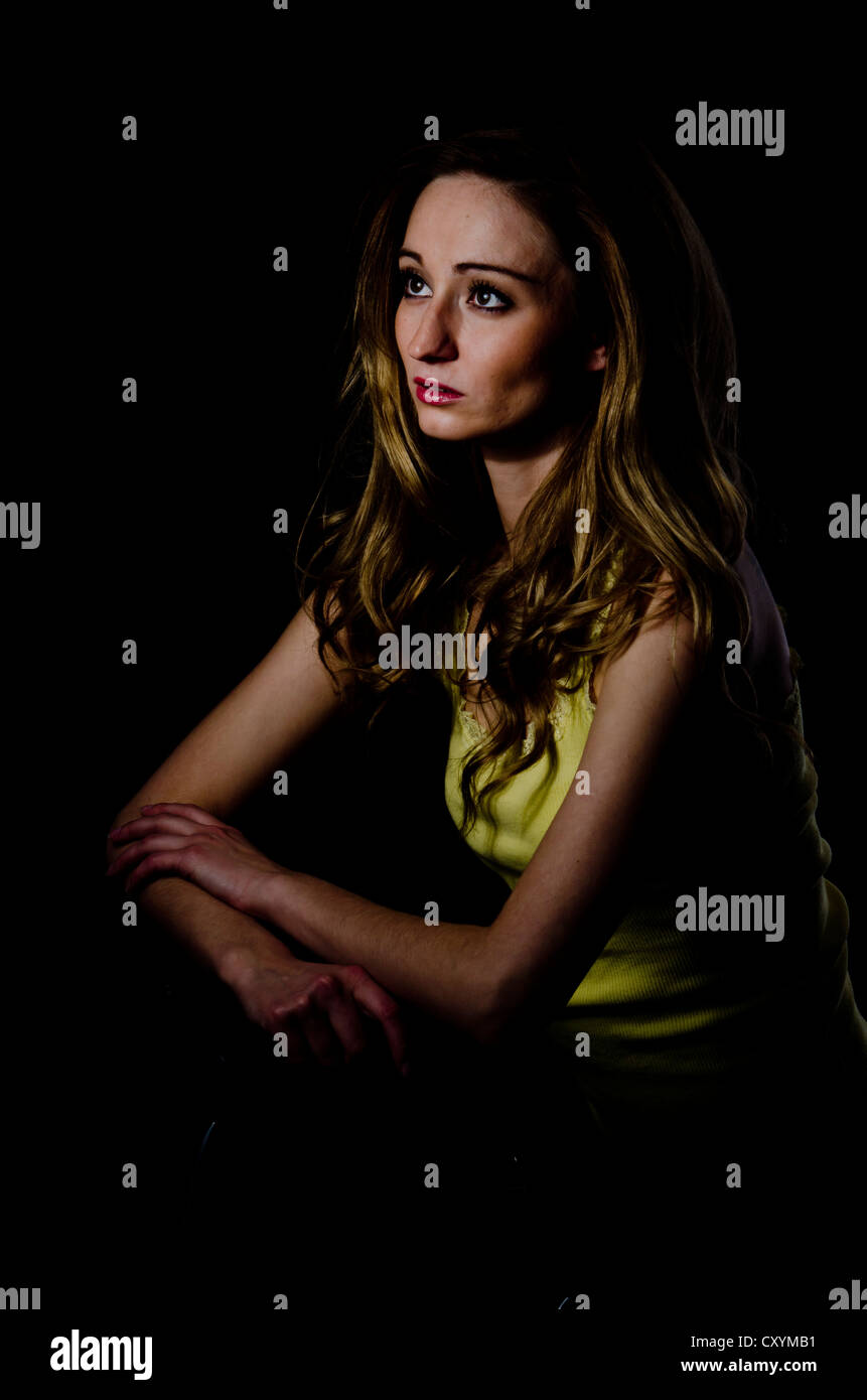 Giovane donna, 25, seduti in un ambiente buio Foto Stock