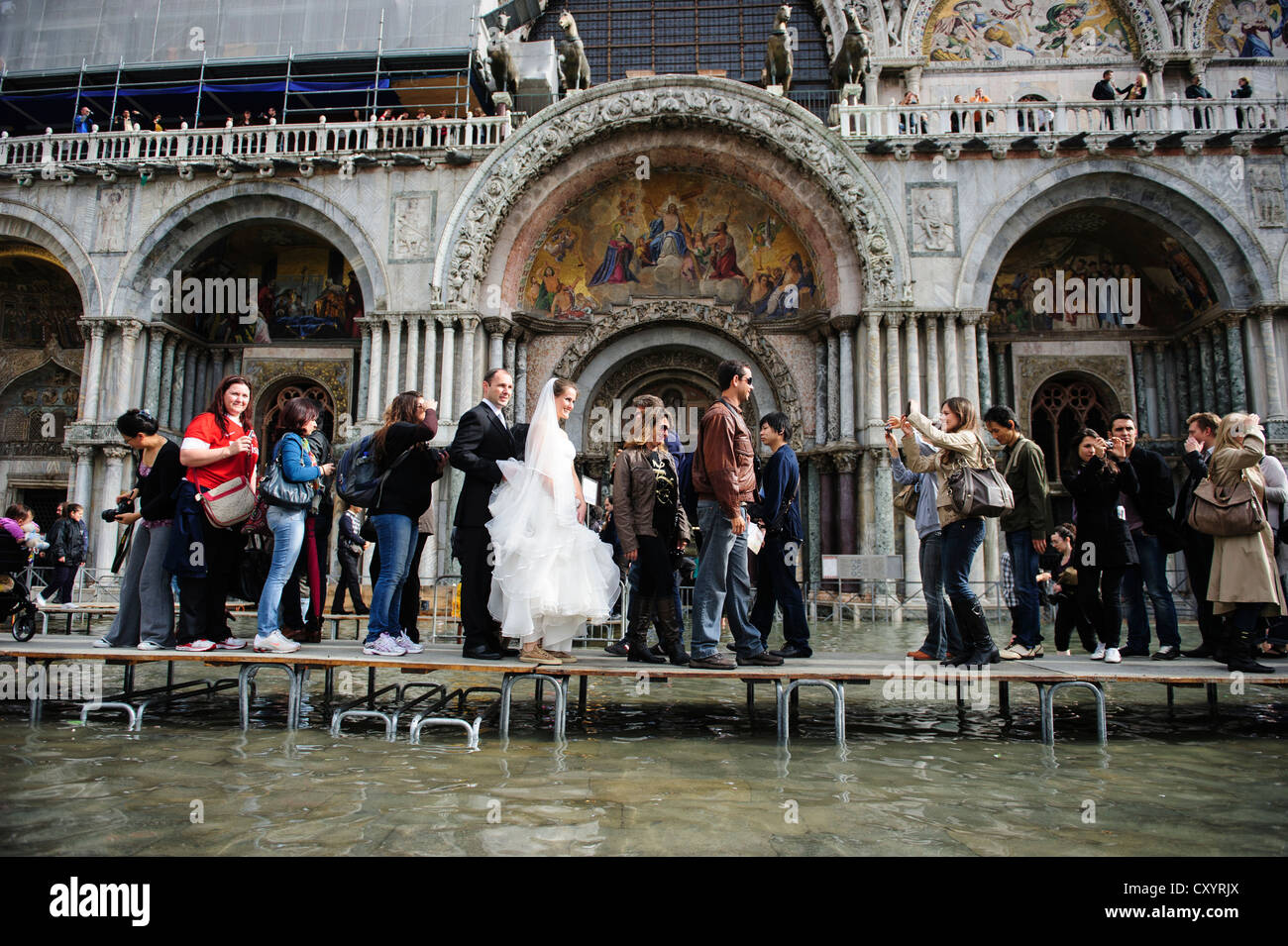 Una coppia sposata a piedi di fronte alla Basilica di San Marco durante il primo giorno del "Acqua Alta stagione a Venezia. Foto Stock