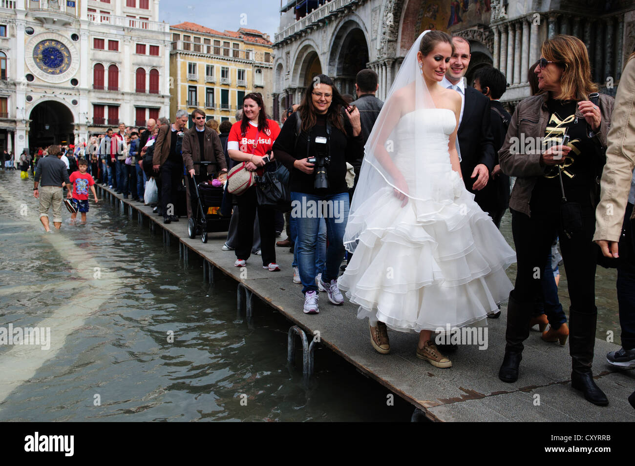 Una coppia sposata a piedi di fronte alla Basilica di San Marco durante il primo giorno del "Acqua Alta stagione a Venezia. Foto Stock
