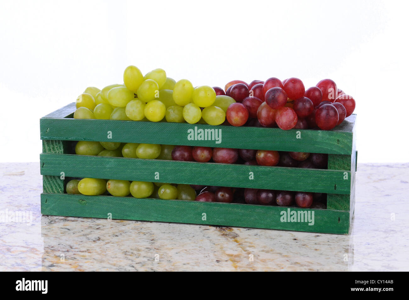 Il rosso e il verde UVA in una cassa di legno su un banco in granito. Formato orizzontale con uno sfondo bianco. Foto Stock