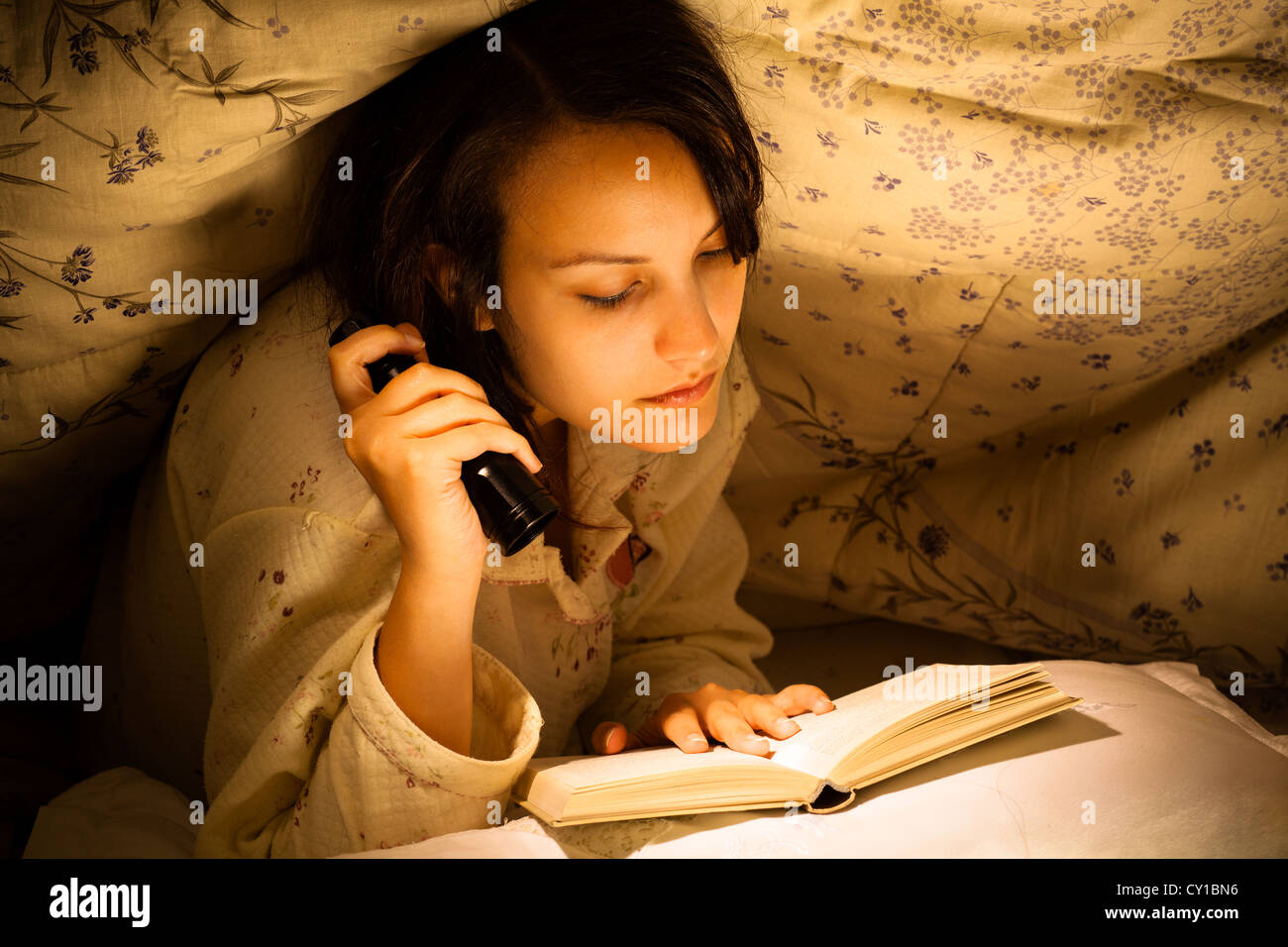 Grave donna la lettura di un libro con la torcia elettrica sul letto Foto  stock - Alamy