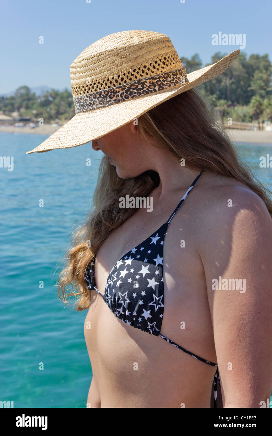 Giovane donna in bianco e nero bikini e cappello di paglia si fermò sulla passerella di legno, guardando il mare. Foto Stock