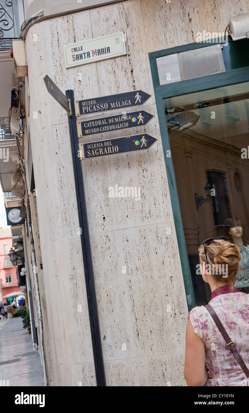Malaga, Costa del Sol, Andalusia. Giovane donna guardando i segni e le indicazioni per raggiungere i siti turistici. Foto Stock