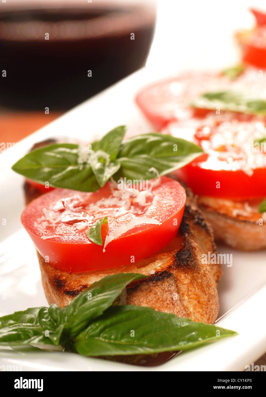 Deliziose bruschette con pomodoro e basilico su un posto bianco con un bicchiere di vino in background. Foto Stock