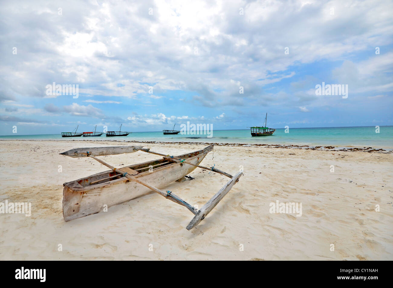 In legno barca di pesca su una spiaggia di Isola di Zanzibar con imbarcazioni turistiche in background su un luminoso giorno di sole. Foto Stock