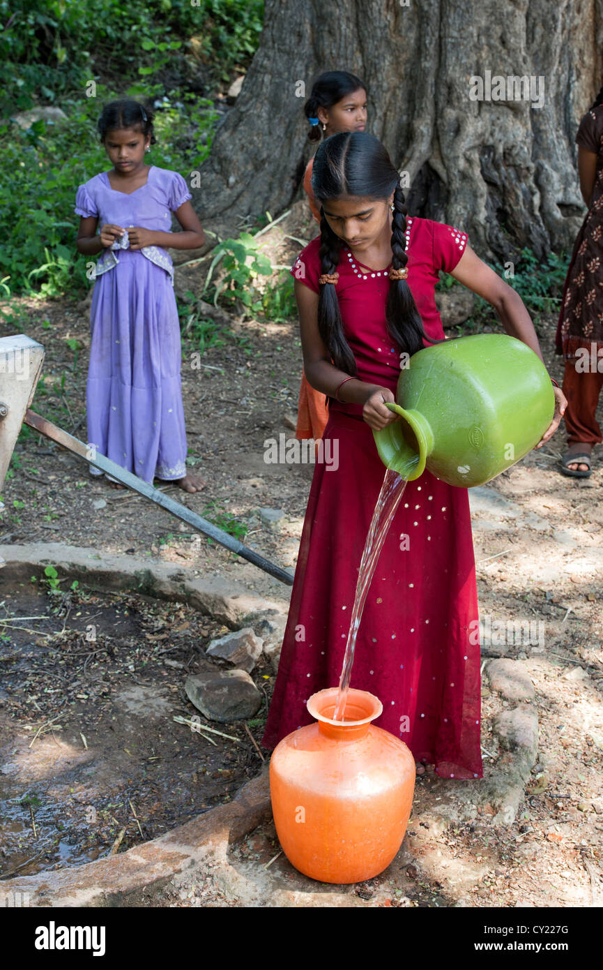 Rurale villaggio indiano ragazza il riempimento di vasi d'acqua da una comune pompa dell'acqua. Andhra Pradesh, India Foto Stock
