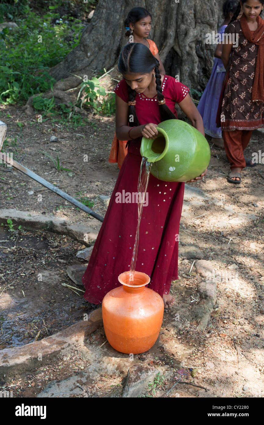 Rurale villaggio indiano ragazza il riempimento di vasi d'acqua da una comune pompa dell'acqua. Andhra Pradesh, India Foto Stock