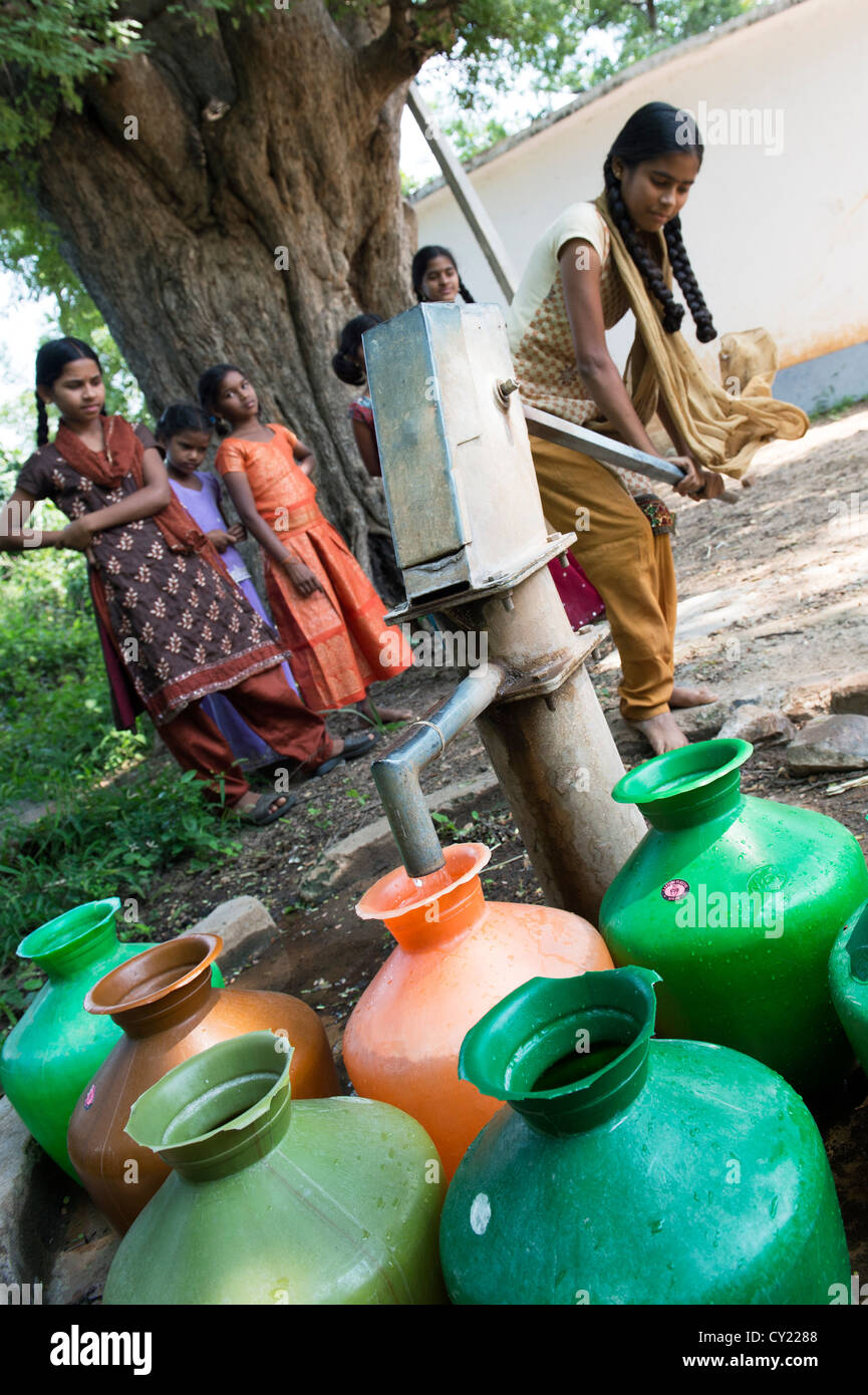 Rurale villaggio indiano ragazza il riempimento di vasi d'acqua da una comune pompa dell'acqua. Andhra Pradesh, India Foto Stock