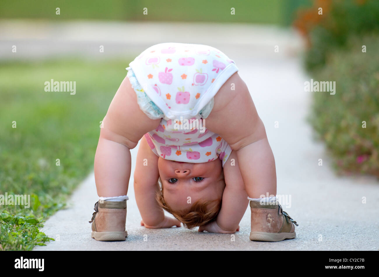 Un anno di bambina giocando a testa in giù sulla strada Foto Stock