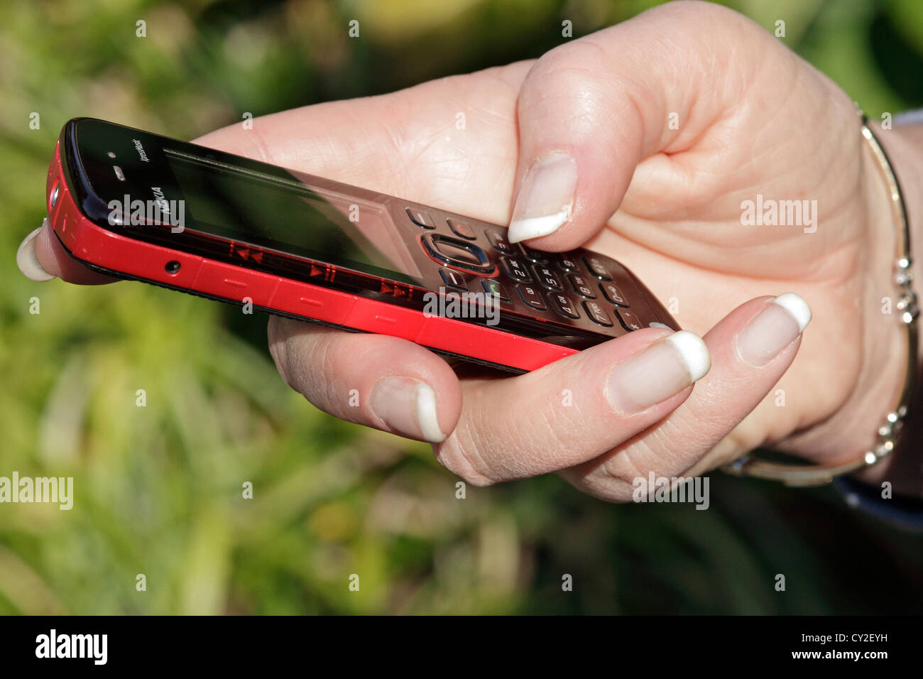 Una donna scrivere messaggi su un rosso telefono cellulare. Foto Stock