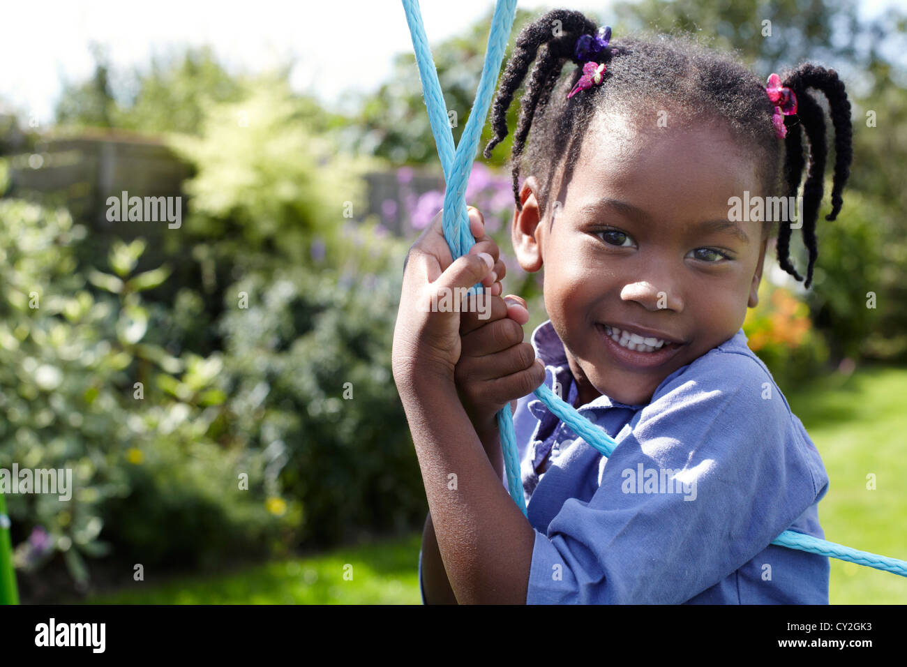 Cinque anni ragazza nera su swing guardando la fotocamera e sorridente Foto Stock