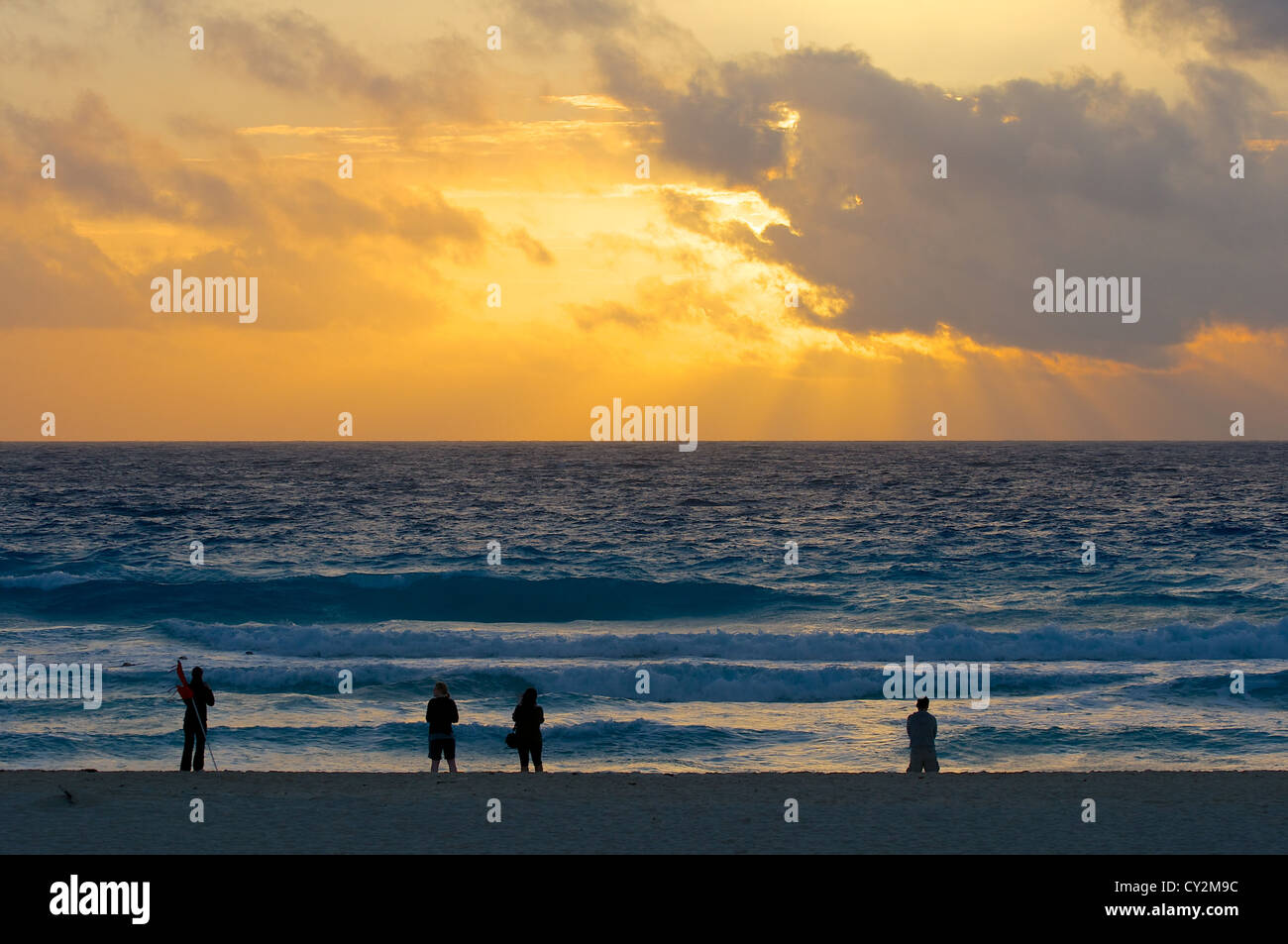 Piccolo gruppo di persone che guardano un golden sunrise su una spiaggia Foto Stock