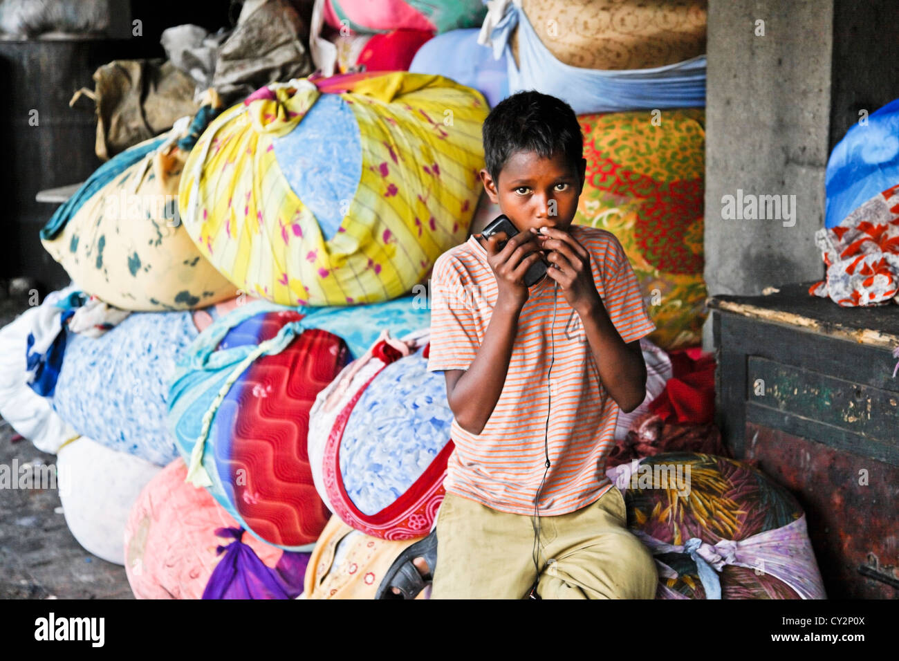 Squallore dell'ufficio commerciale per bucato per lavaggio a mano a Bombay, un ragazzo detiene sul suo telefono cellulare guardando la lente delle balle di vestiti Foto Stock