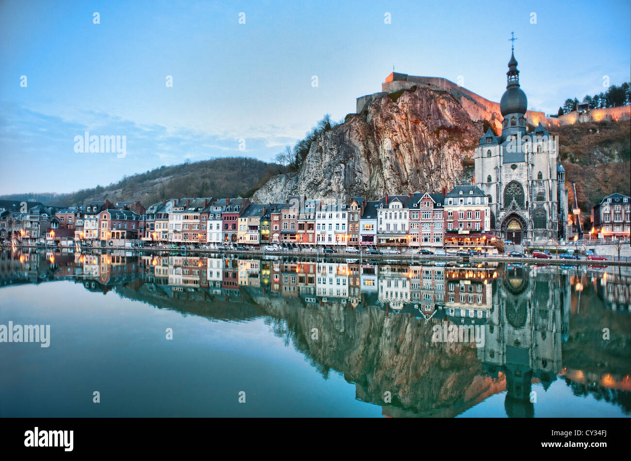 Case, negozi, una chiesa e una fortezza si riflettono nel fiume Meuse al tramonto nella città belga di Dinant nelle Ardenne Foto Stock