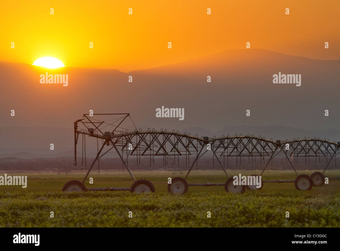 Il sole tramonta dietro un braccio di irrigazione a spirale in terreni agricoli nella valle del Sacramento, California. Foto Stock