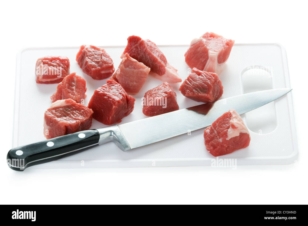 Materie carne di agnello tagliato a dadini con il coltello da cucina e tagliere isolato su uno sfondo bianco Foto Stock