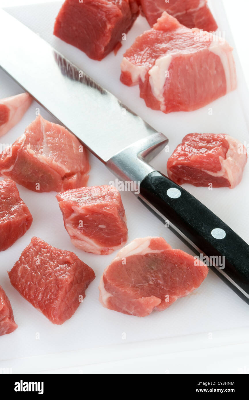 Materie carne di agnello tagliato a dadini con il coltello da cucina e tagliere Foto Stock