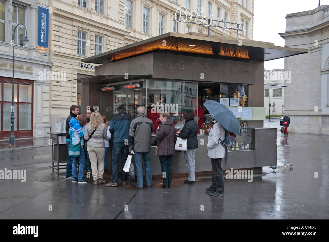 Turisti affamati stanno intorno un wurstel/hot dog fast food chiosco di Vienna in Austria. Foto Stock