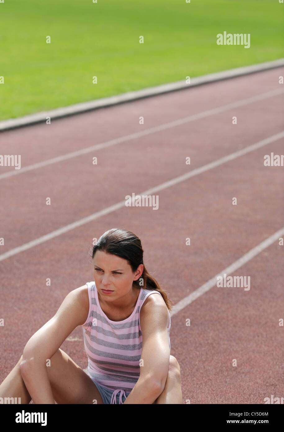 Atletica Giovane sportive, seduto da solo sulla traccia di cenere in stadium dopo o prima della competizione sportiva e guardare l'opposizione Foto Stock