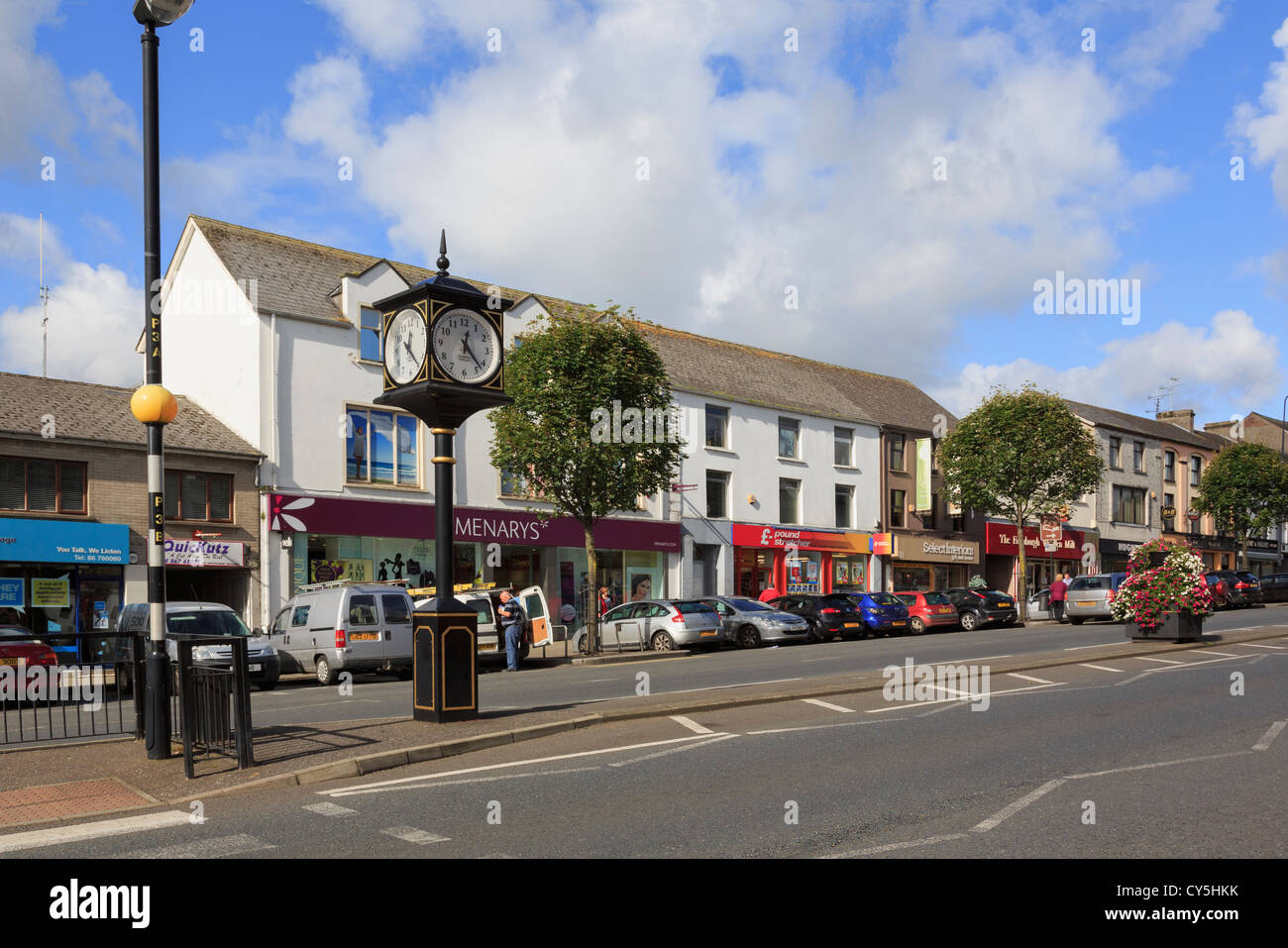 Guardando attraverso ampia strada principale per la citta' orologio e negozi con le auto parcheggiate sul ciglio della strada in Cookstown County Tyrone Irlanda del Nord Regno Unito Foto Stock