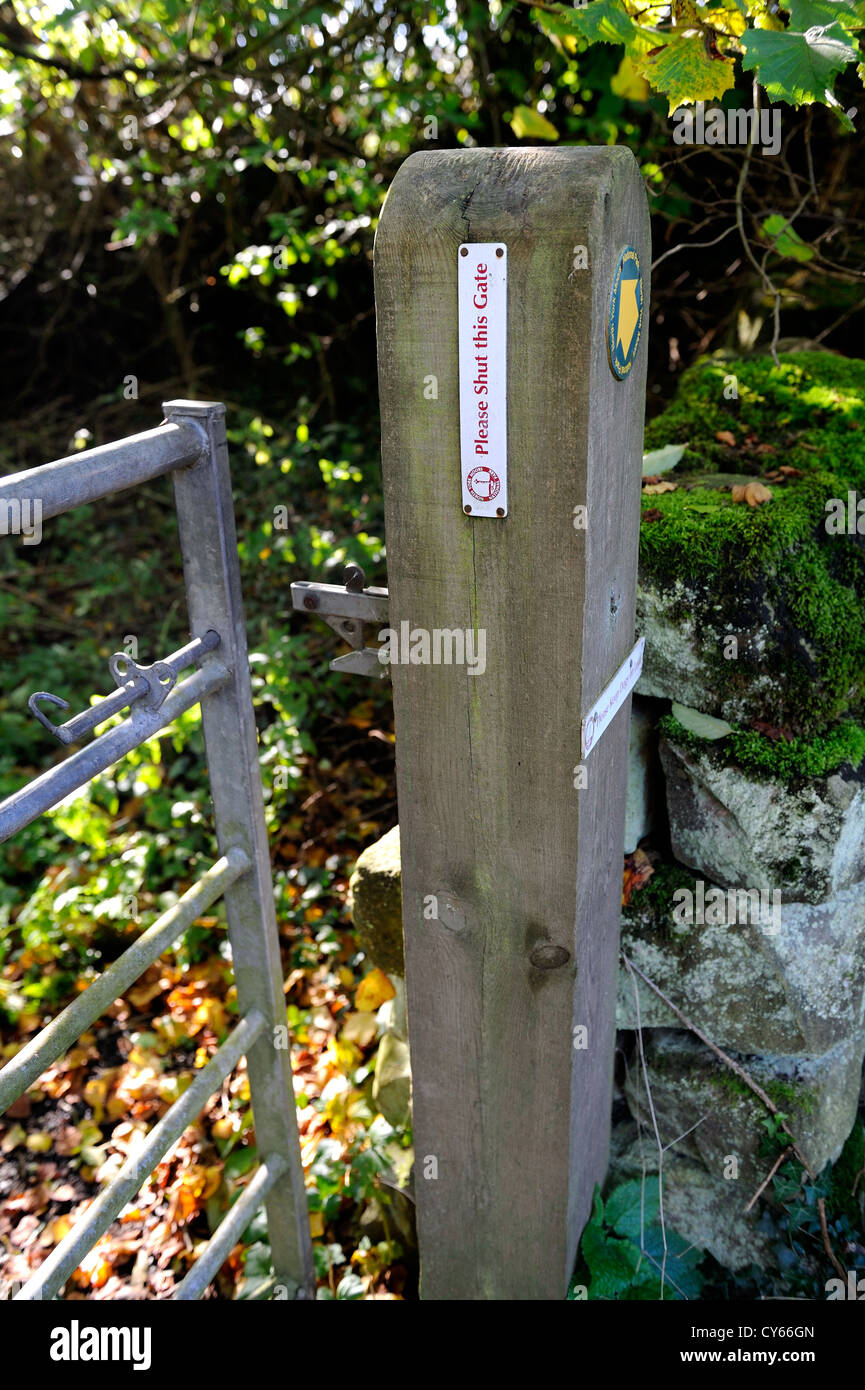 Cancello in legno post e porta di metallo che conduce a un sentiero pubblico con un cartello si prega di chiudere il portone. Foto Stock