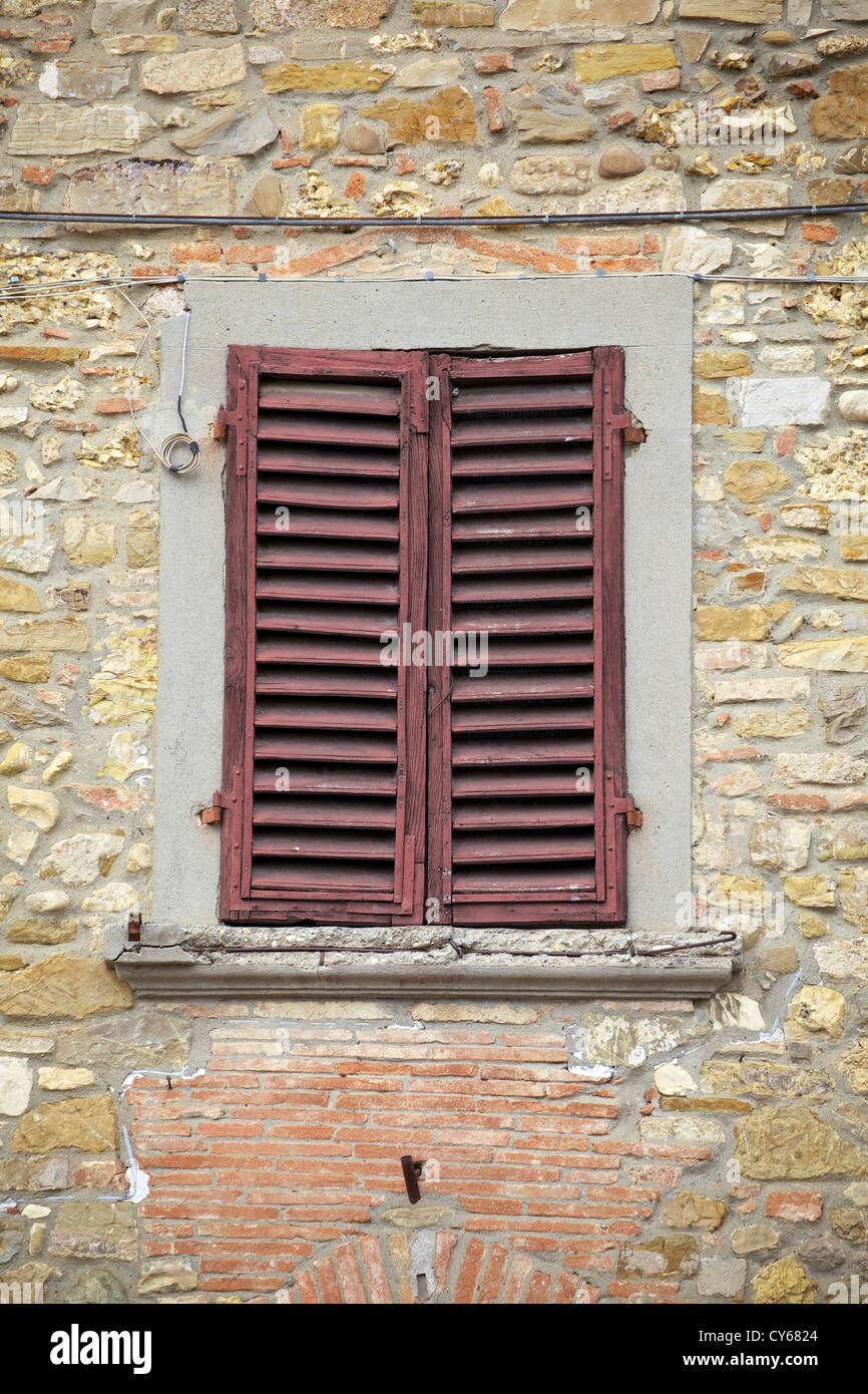 Rustico rosso spiovente persiane alle finestre contro una pietra e mattoni Parete strutturata in Toscana Foto Stock