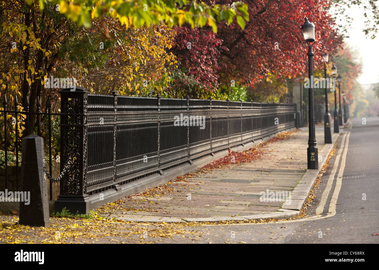 Una recinzione metallica e la fila di pali della luce su un marciapiede sul cerchio esterno di Regent's Park, Londra, Inghilterra, Regno Unito. Foto Stock