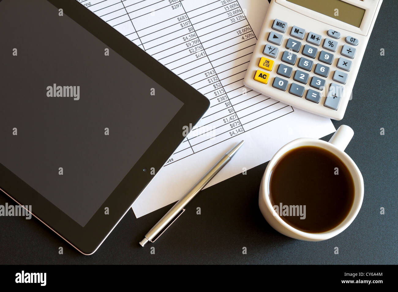 Ambiente di lavoro moderno con tavoletta digitale che mostra grafici e schema sullo schermo, caffè, penna e carta con i numeri. Foto Stock