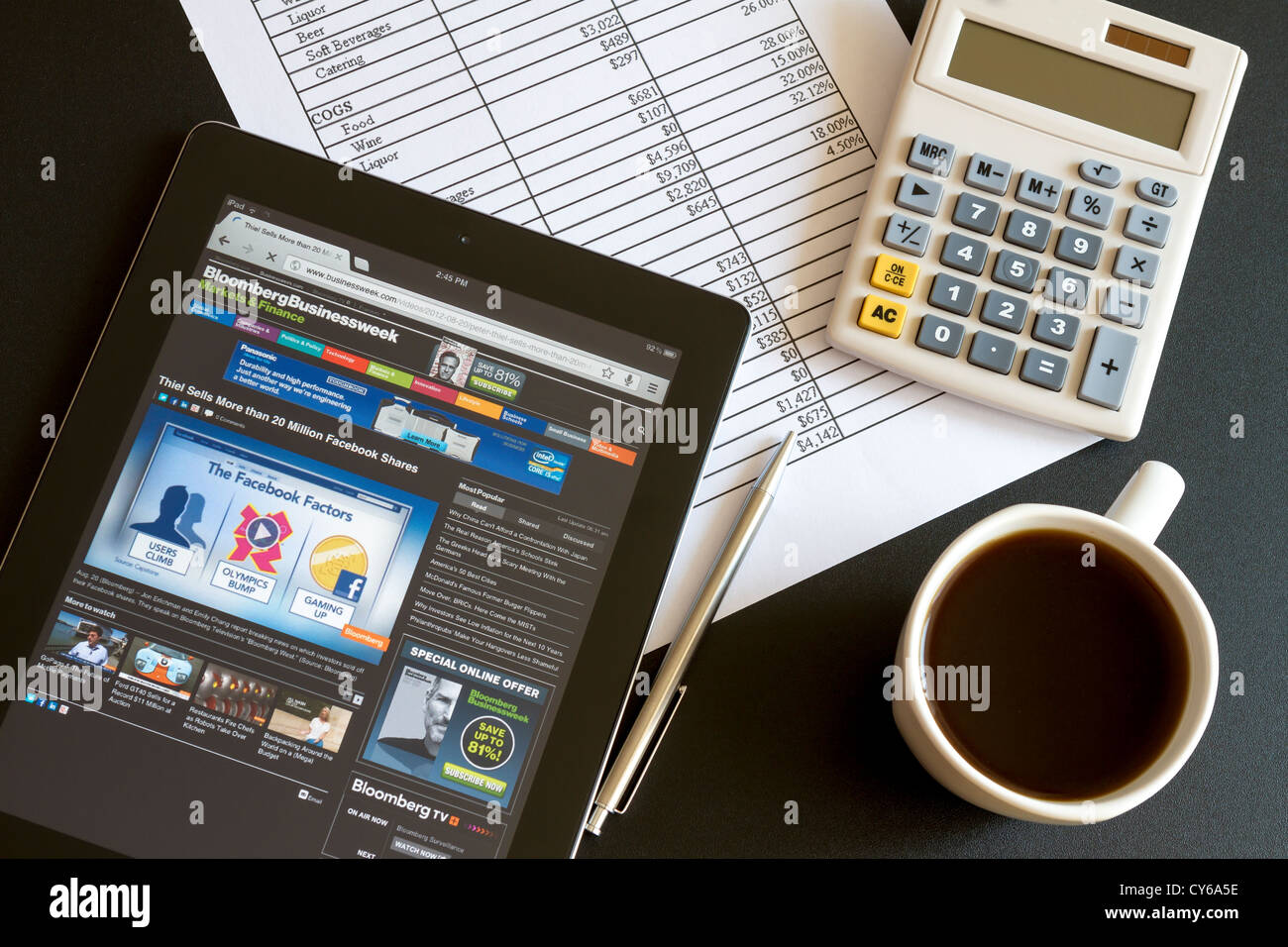 Ambiente di lavoro moderno con ipad 3 mostra grafici e schema sullo schermo, caffè, penna e carta con i numeri. Foto Stock