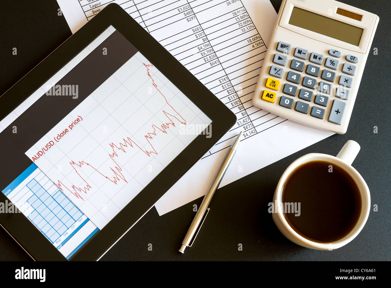 Ambiente di lavoro moderno con tavoletta digitale che mostra grafici e schema sullo schermo, caffè, penna e carta con i numeri. Foto Stock