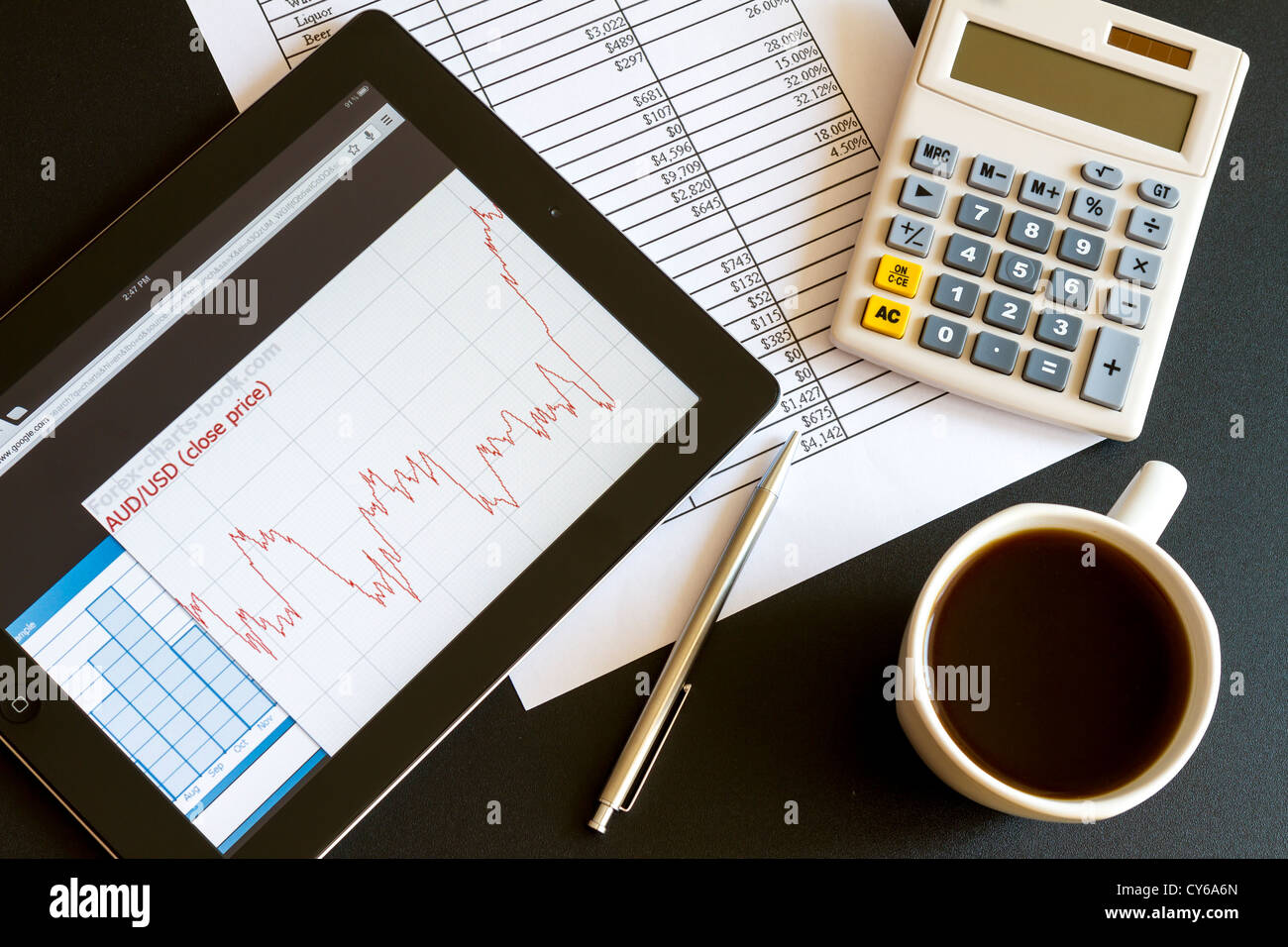 Ambiente di lavoro moderno con tavoletta digitale che mostra grafici e schema sullo schermo, caffè, penna e carta con i numeri. Foto Stock
