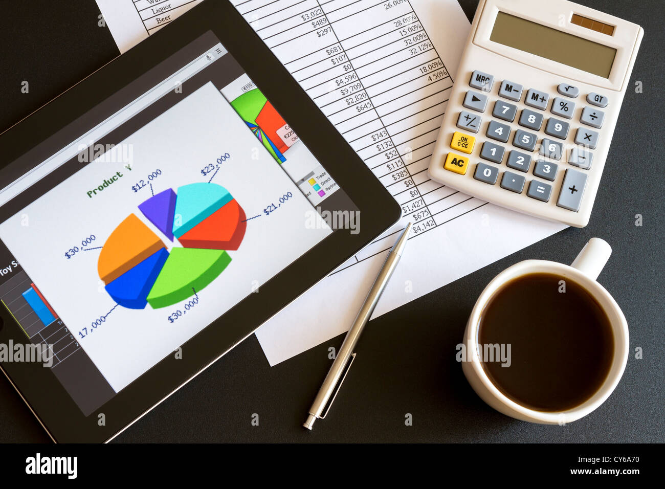 Ambiente di lavoro moderno con tavoletta digitale che mostra grafici e schema sullo schermo, caffè, penna e carta con i numeri. Foto Stock
