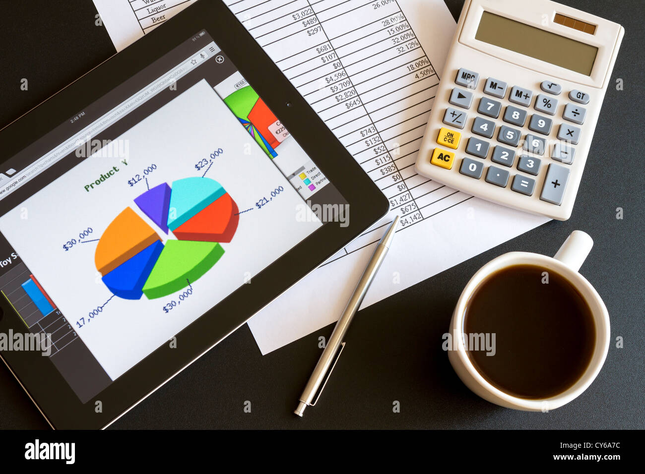 Ambiente di lavoro moderno con tavoletta digitale che mostra grafici e schema sullo schermo, caffè, penna e carta con i numeri. Foto Stock