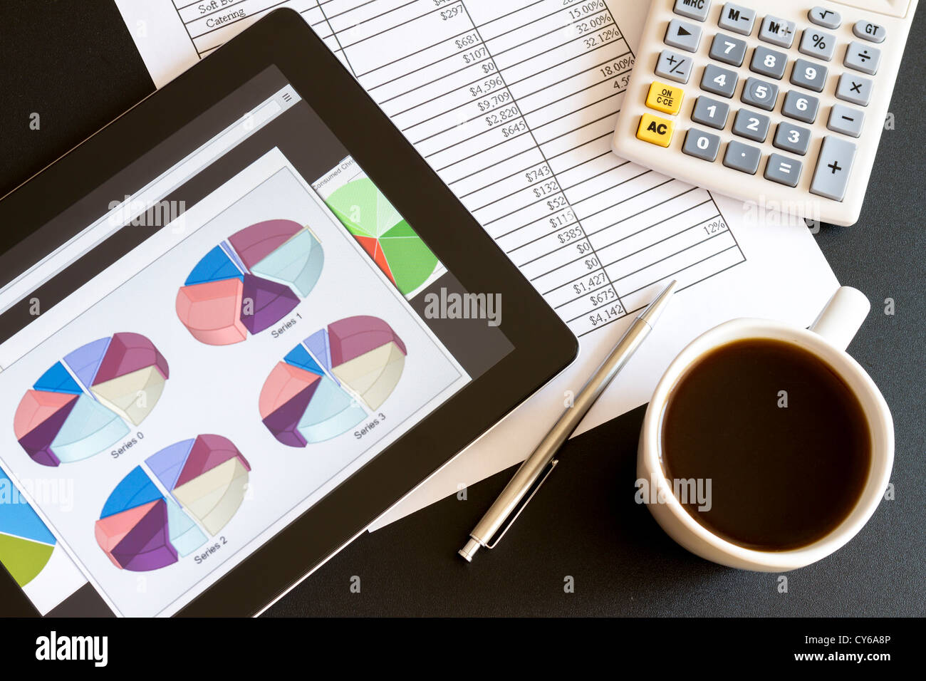 Ambiente di lavoro moderno con tavoletta digitale che mostra grafici e schema sullo schermo, caffè, penna e carta con i numeri. Foto Stock