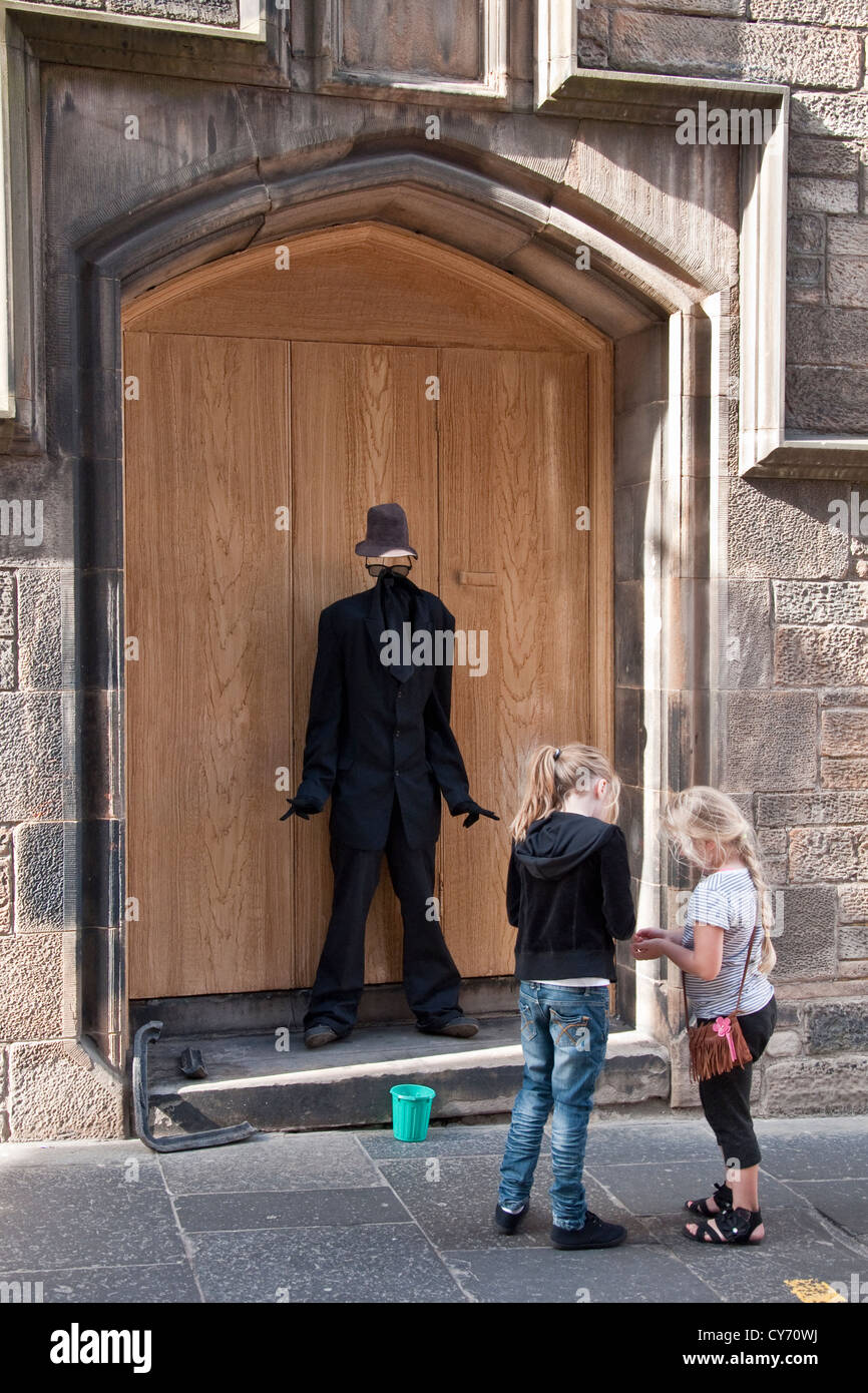 Le ragazze giovani dando soldi di tasca per 'Uomo Invisibile' street agiscono sul Royal Mile nel centro storico di Edimburgo Foto Stock