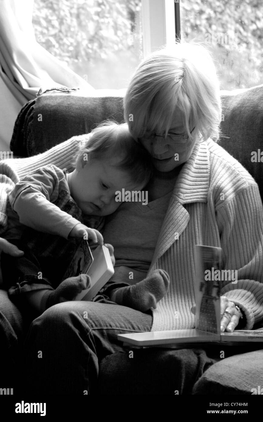 Bianco e nero fotografia di famiglia di nonna la lettura per la sua giovane nipote e dandogli una coccola mentre è seduto in poltrona Foto Stock
