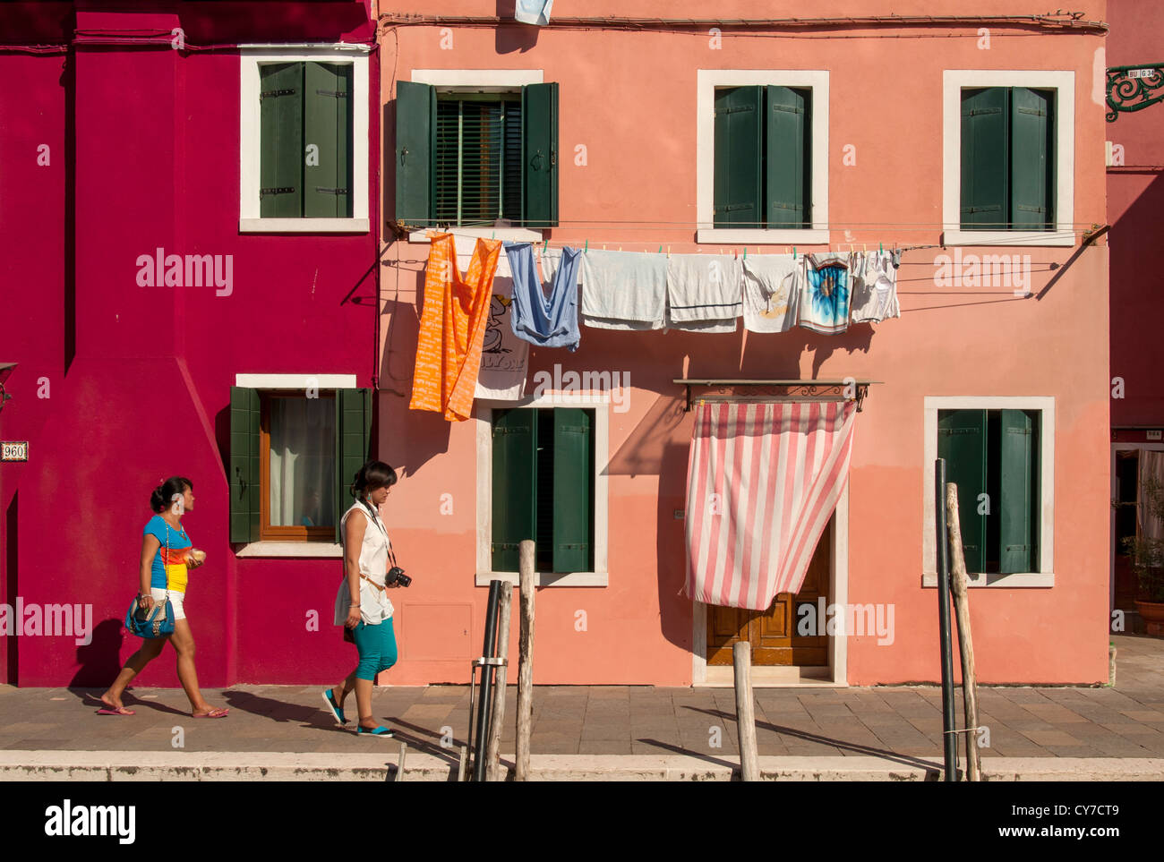 Due giovani donne passano dipinto luminosamente case, Burano, Venezia, Veneto, Italia Foto Stock