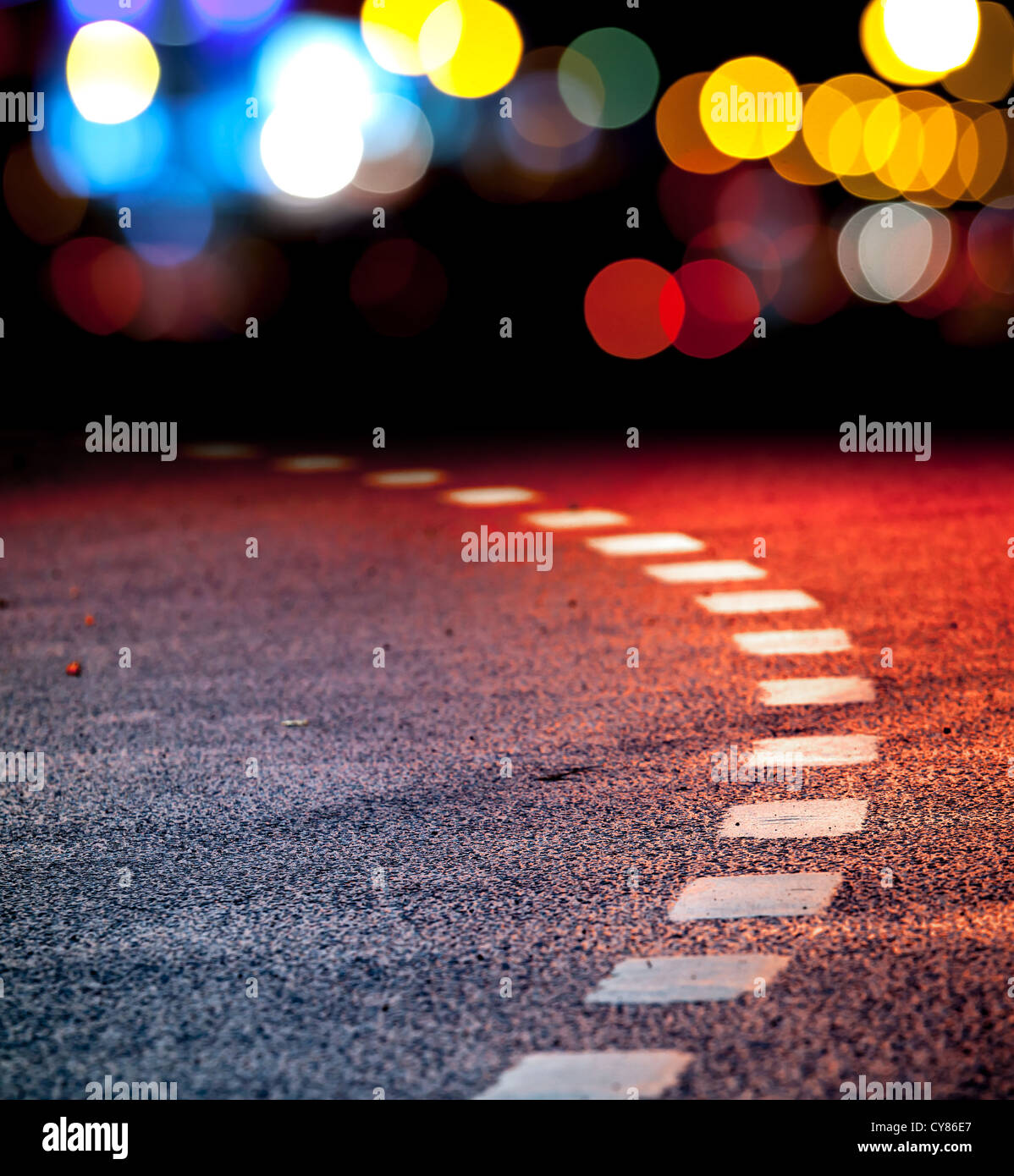 Girando strada asfaltata con linee di marcatura e di riflessioni con colorate luci non focalizzato su uno sfondo Foto Stock