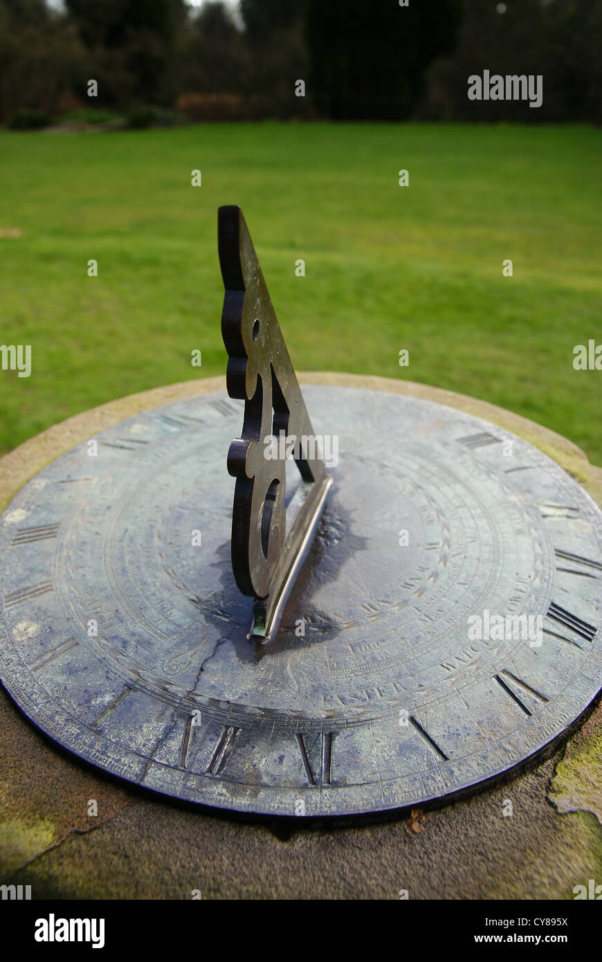 Un orologio solare su uno zoccolo in pietra in un ambiente da giardino Foto Stock